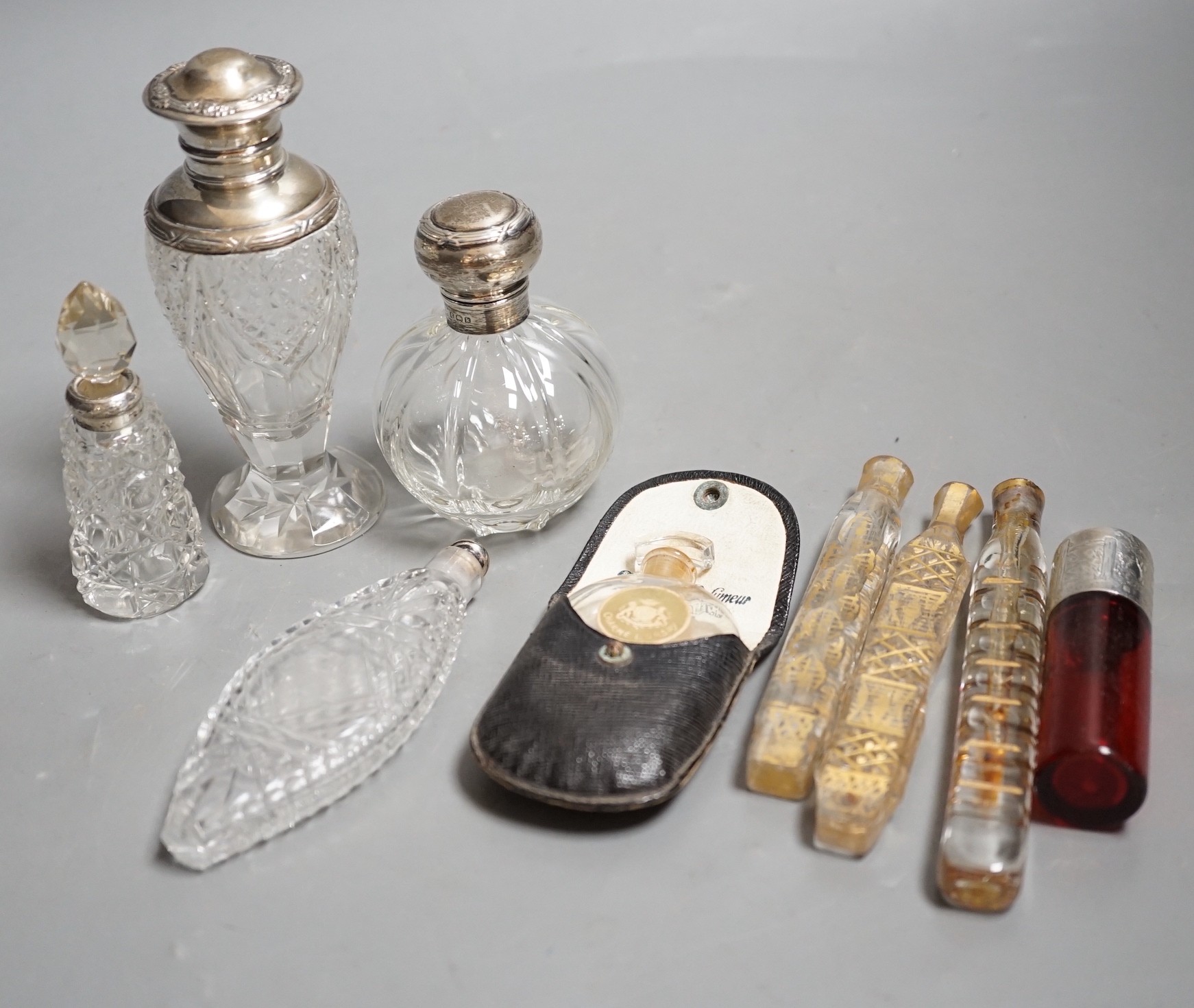 A late Victorian silver mounted ruby glass cylindrical scent bottle, engraved in the style of Kate Greenaway, Sampson Mordan & Co, London, 1887, 75mm, together with eight other assorted glass scent bottles, three with si